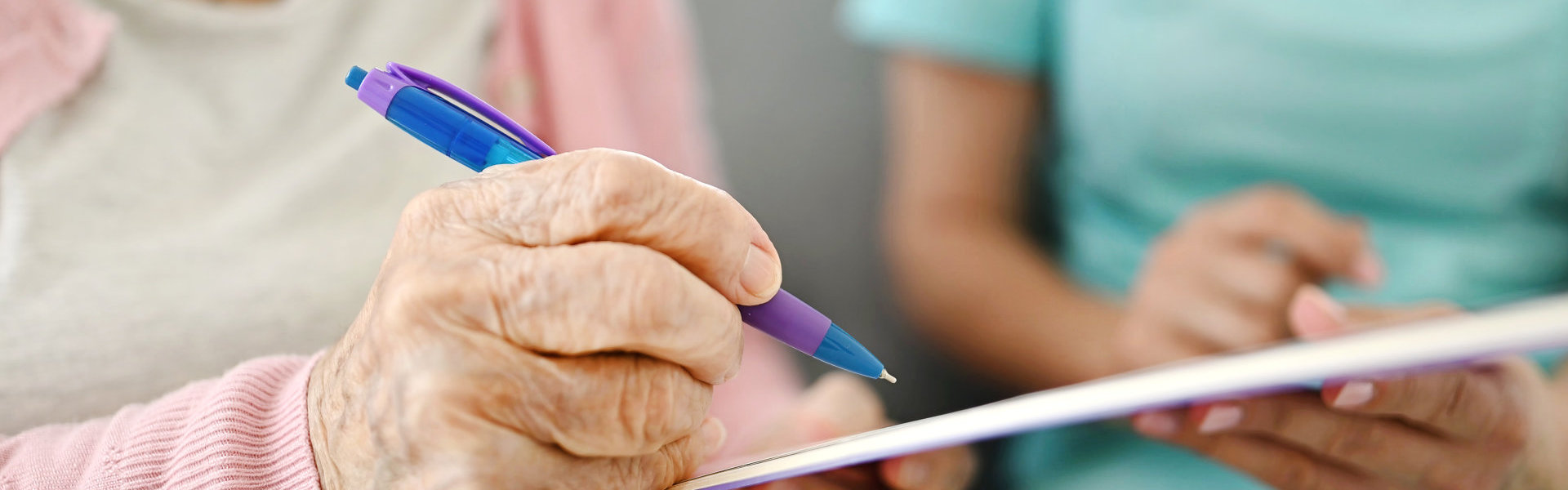 Elderly Woman Signs Document With Assistant Nearby